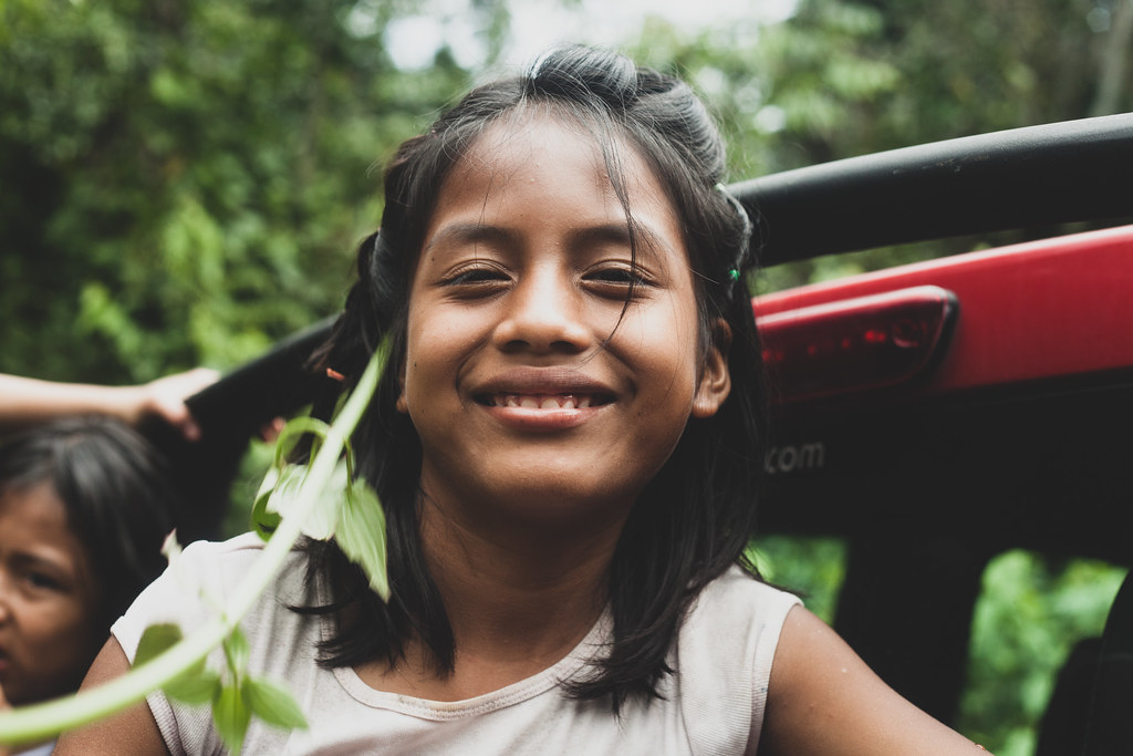 Una niña sonríe con los ojos cerrados, al aire libre